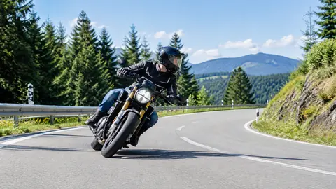 Motorradfahrer in Schräglage blickt mit gedrehtem Kopf zum Kurvenausgang