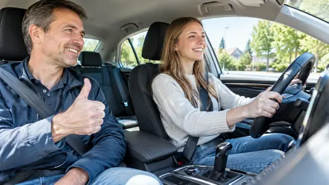 Fahrschülerin am Steuer eines Automatikautos, der Fahrlehrer zeigt den Daumen nach oben