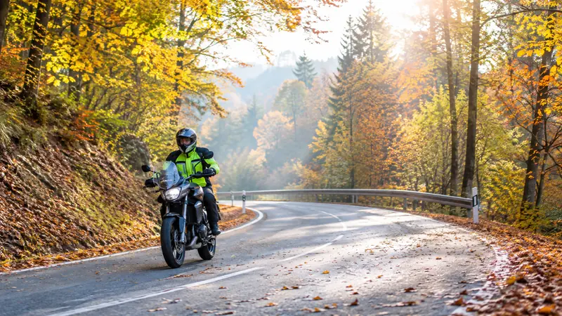 Motorradfahrer fährt vorsichtig über eine mit Herbstlaub bedeckte Waldstraße