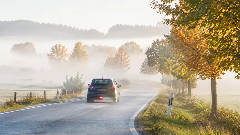 Ein Auto fährt mit eingeschalteter Nebelschlussleuchte über eine neblige Landstraße